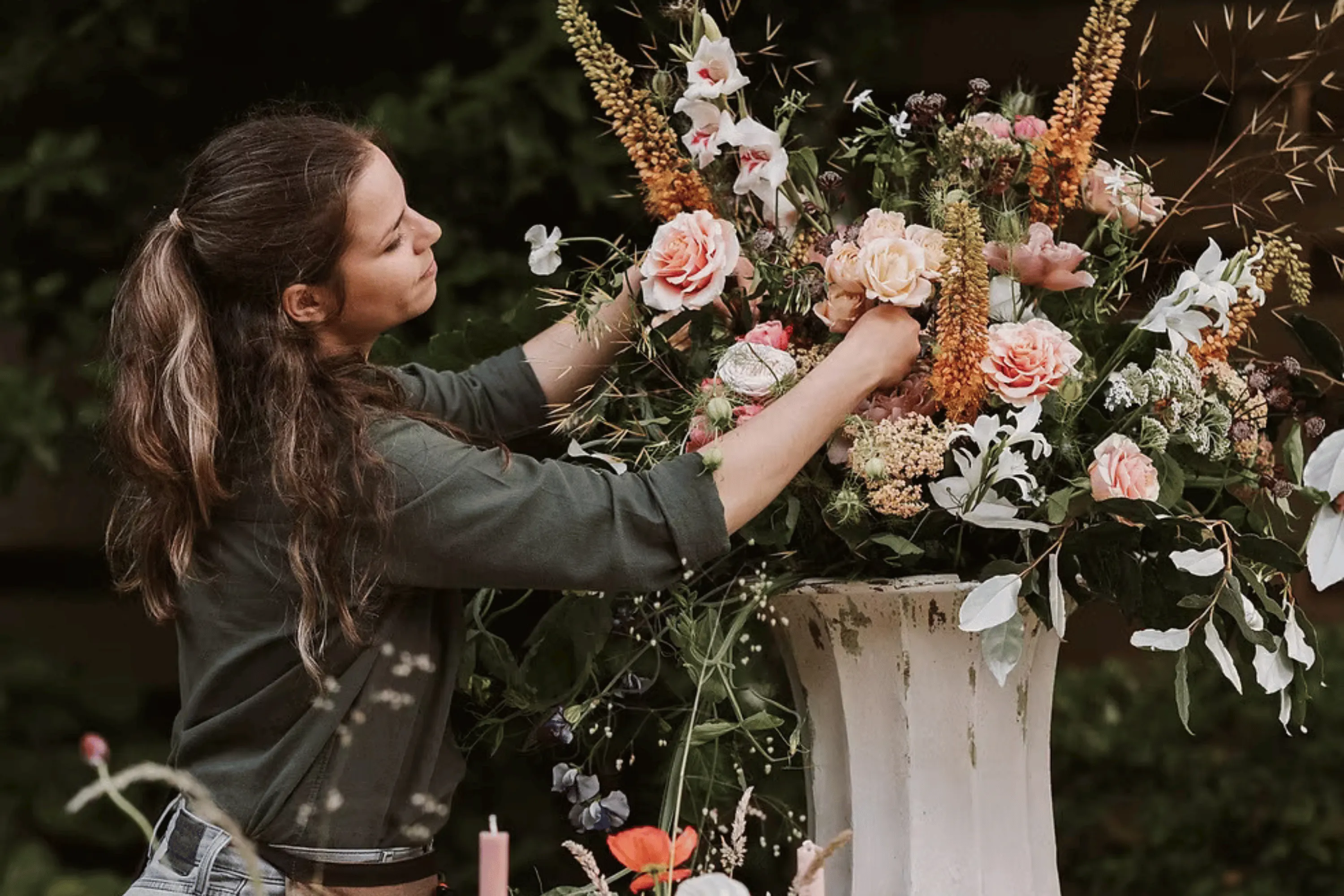 A florist arranging a large pedestal display of roses and summer flowers.